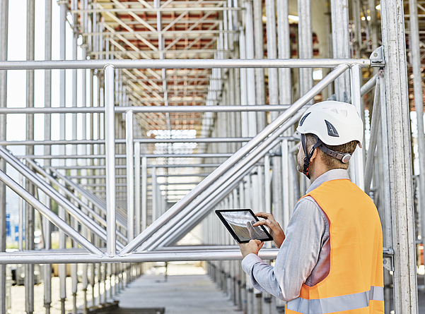 Architekt mit Tablet auf Baustelle Ein Architekt mit Schutzhelm steht mit einem Tablet in der Hand auf einer Baustelle.